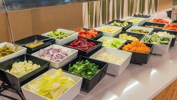 A buffet with various food items in trays, including vegetables, fruits, and salads.