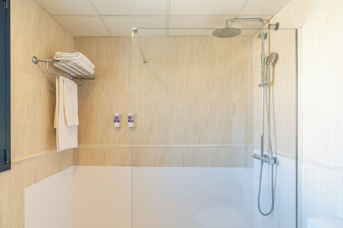 Un área de ducha moderna con mampara de vidrio, ducha de mano y toallero de pared.