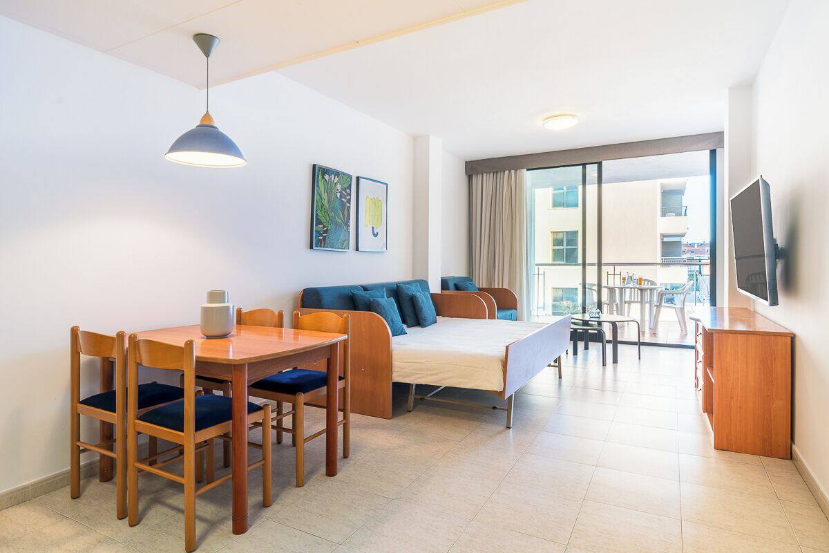 Een moderne hotelkamer met een bed, een eettafel met stoelen, een televisie en een balkon met uitzicht.