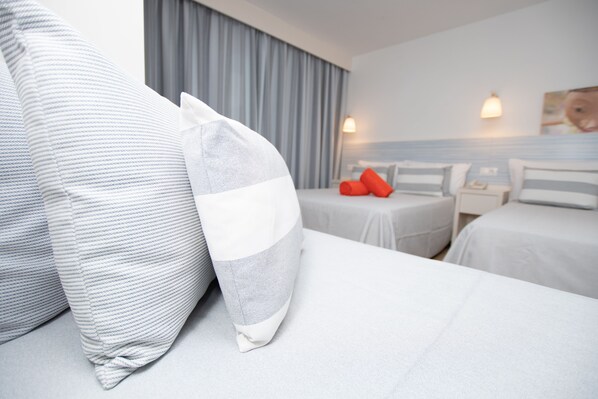 A hotel room with two beds, a nightstand, and a wall-mounted lamp.