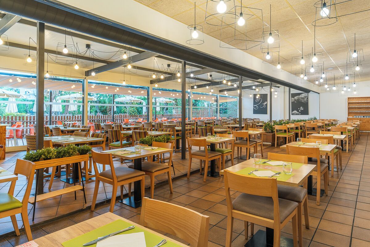 A spacious restaurant with multiple dining areas, large windows, and hanging light fixtures.