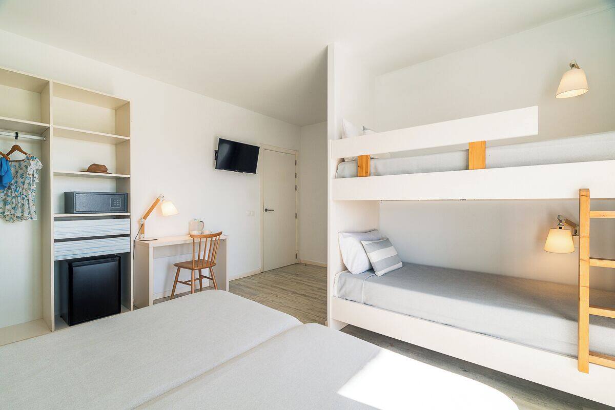 Een compacte kamer met stapelbedden, een bureau met stoel, een televisie en een kleine koelkast.