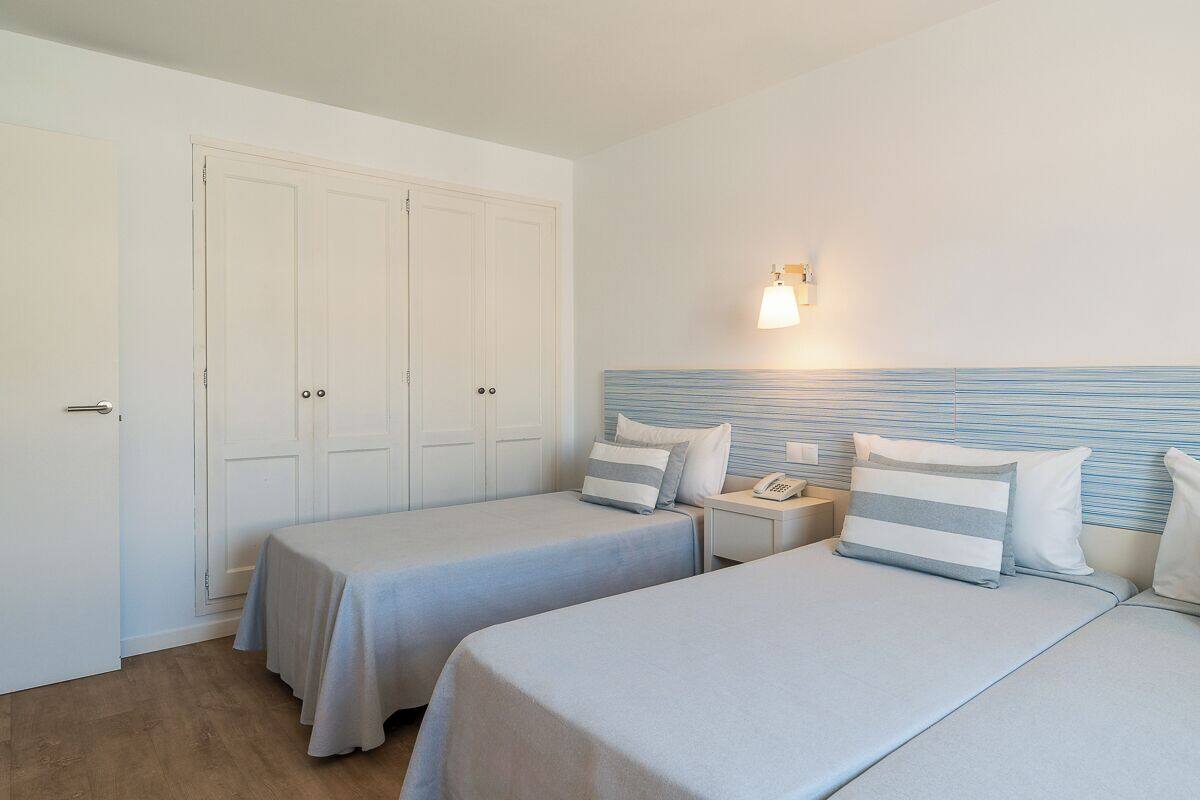 Een hotelkamer met twee bedden, een kledingkast, een nachtkastje met lamp en een telefoon.