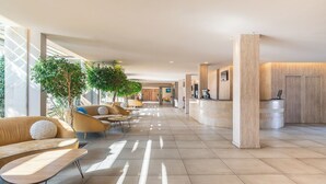 A spacious lobby with a modern design, featuring a reception desk, seating area with sofas and chairs, and large windows allowing natural light.