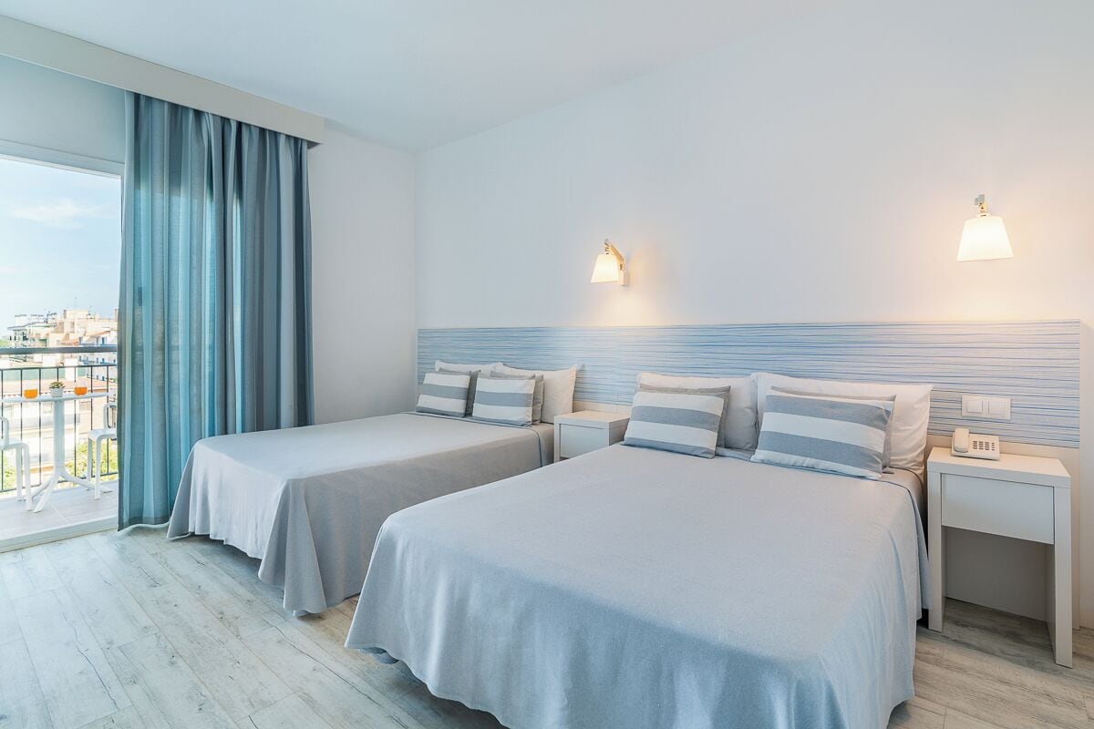 Habitación de hotel con dos camas, un balcón con vistas y un paisaje urbano a la vista a través de la ventana.