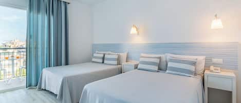 Habitación de hotel con dos camas, un balcón con vistas y un paisaje urbano a la vista a través de la ventana.