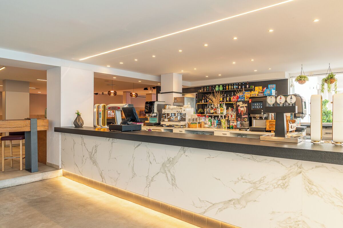 A modern bar area with a marble countertop, espresso machines, and a variety of bottles and glasses.