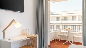 A hotel room with a desk, chair, and a large window with a balcony view.