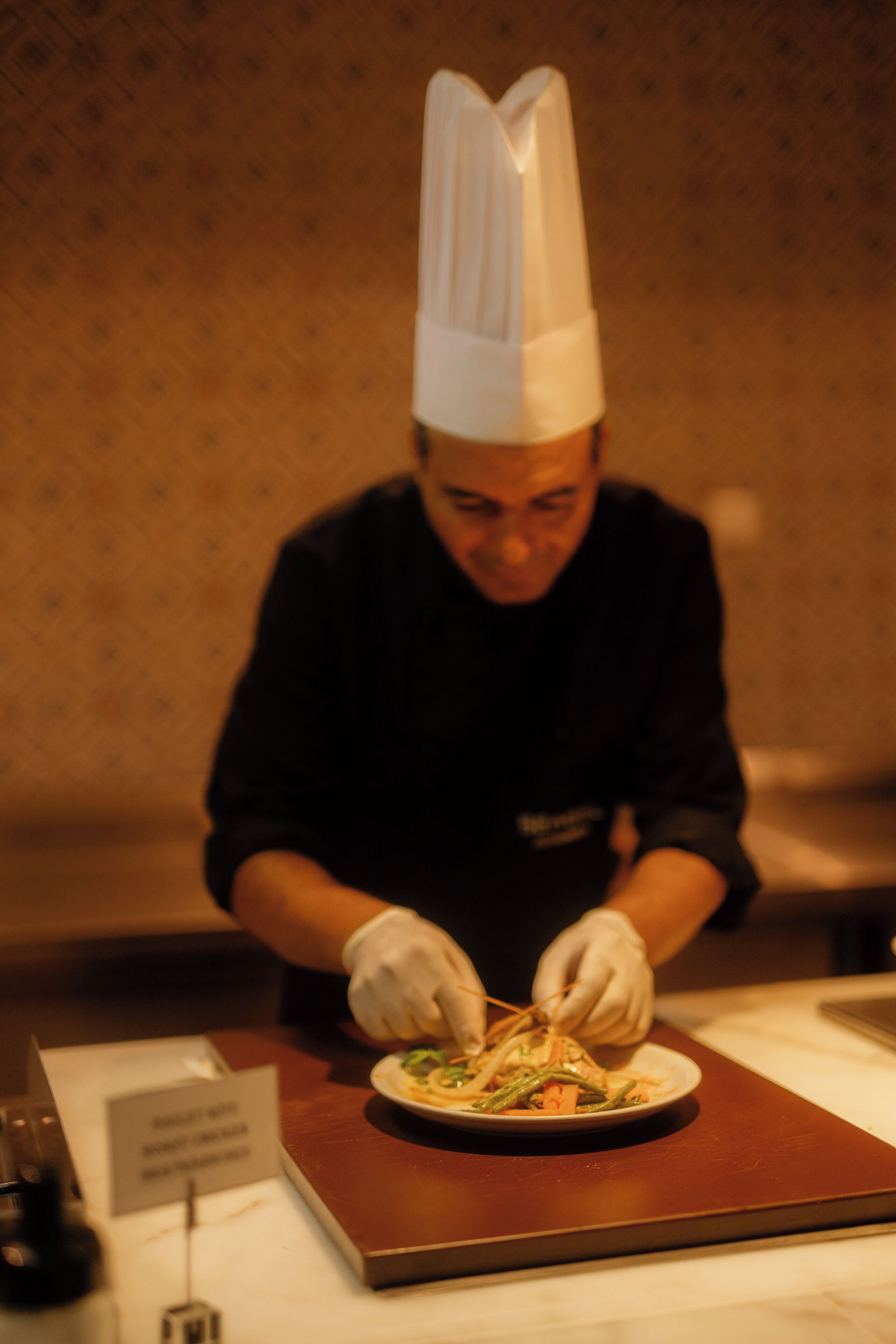 Una persona con gorro y guantes de chef, preparando comida en un plato.