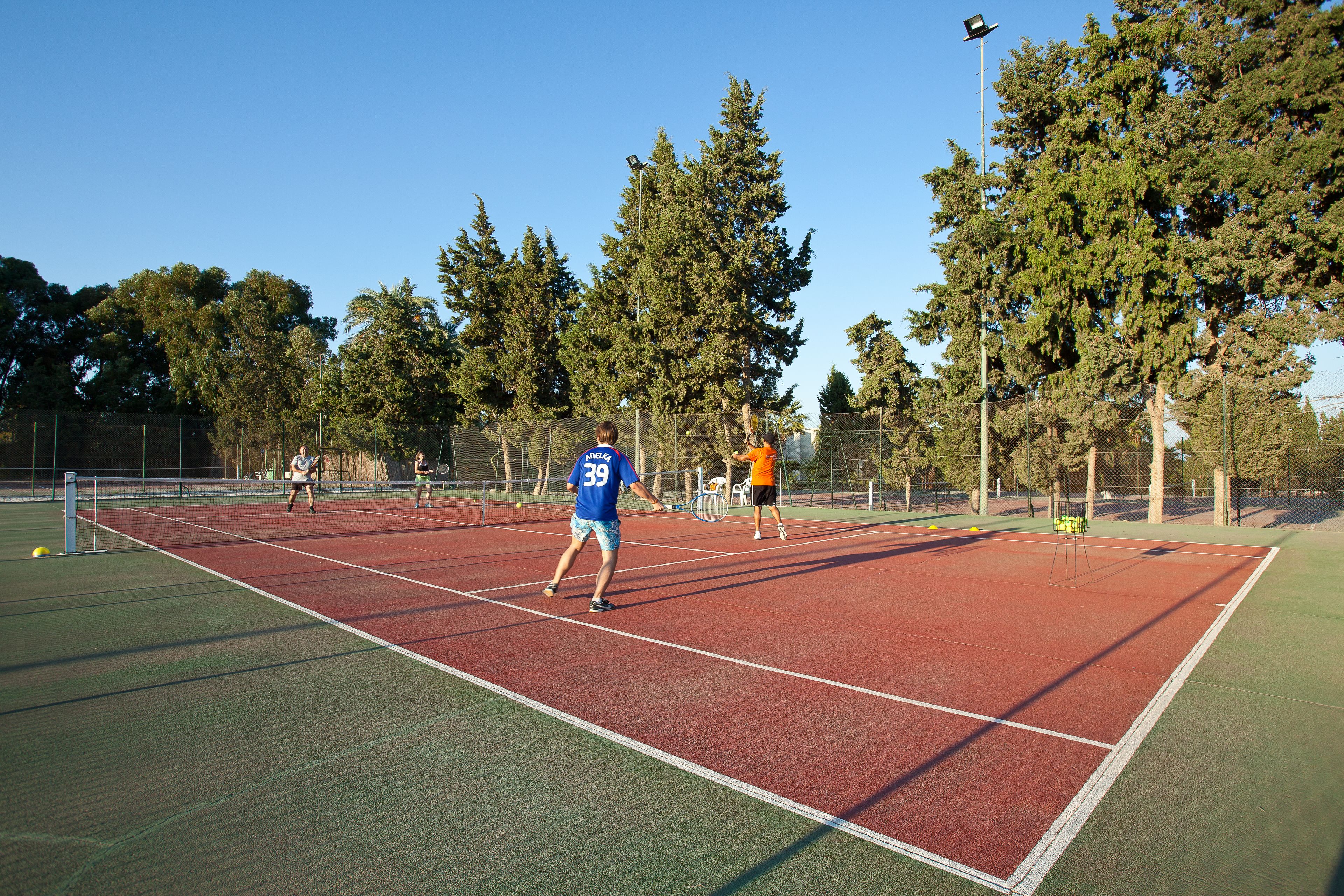Ein Tennisplatz mit Netz, umgeben von Bäumen und einem Zaun.