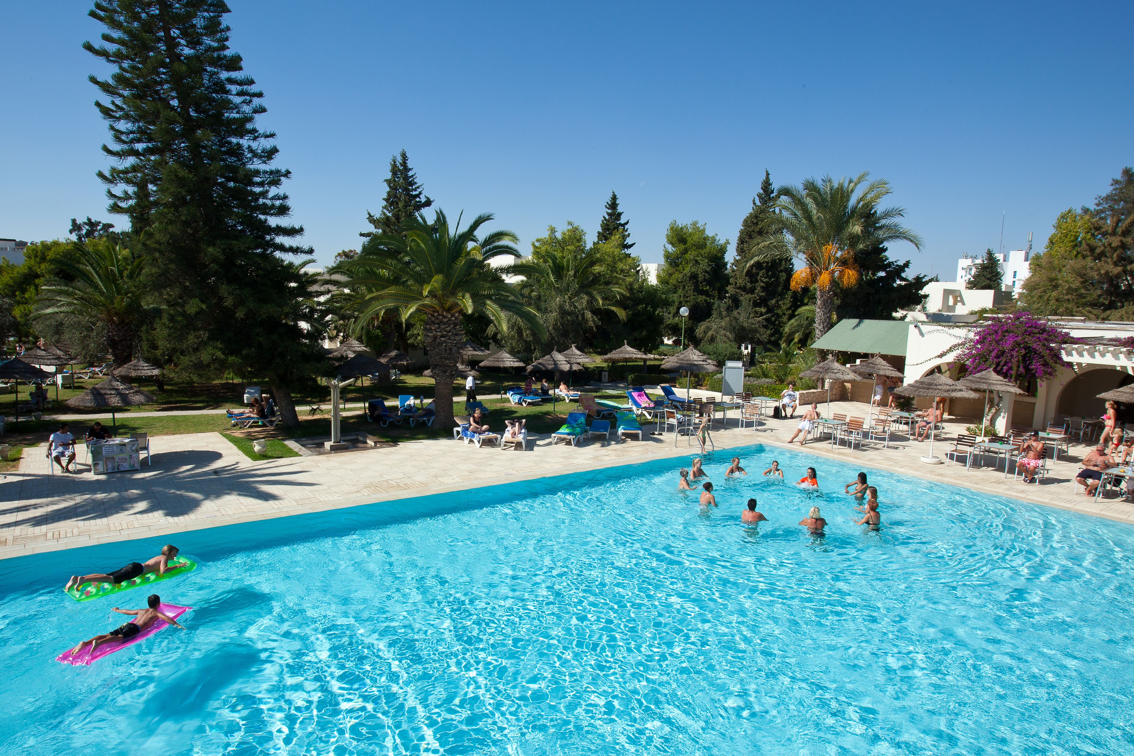 Una piscina con gente nadando y tomando el sol.