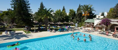 Una piscina con gente nadando y tomando el sol.