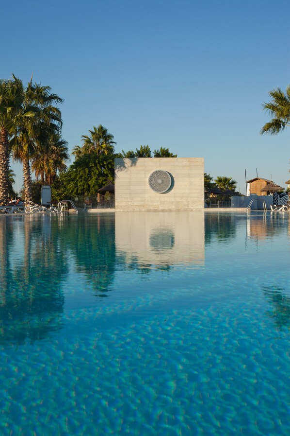 A clear blue pool with a decorative wall in the center, surrounded by palm trees and lounge chairs. - Seabel Alhambra Beach Golf & Spa (Port El Kantaoui)
