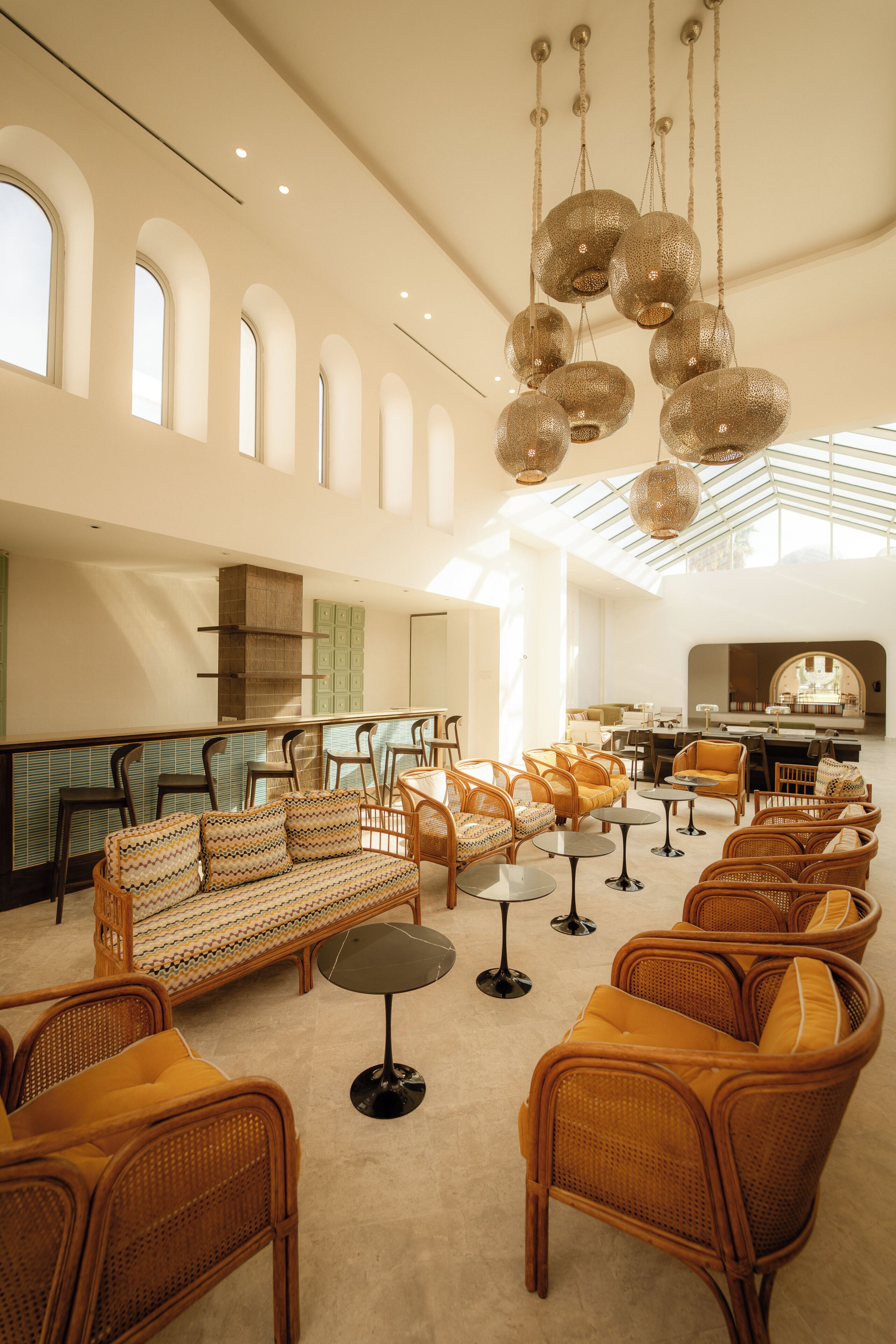 A spacious lobby with a high ceiling, wicker furniture, and a modern chandelier.