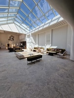 Ein großzügiger Wohnbereich mit hoher Decke und Oberlicht, ausgestattet mit einem modernen Sofa, einer Sitzbank und einem Essbereich.