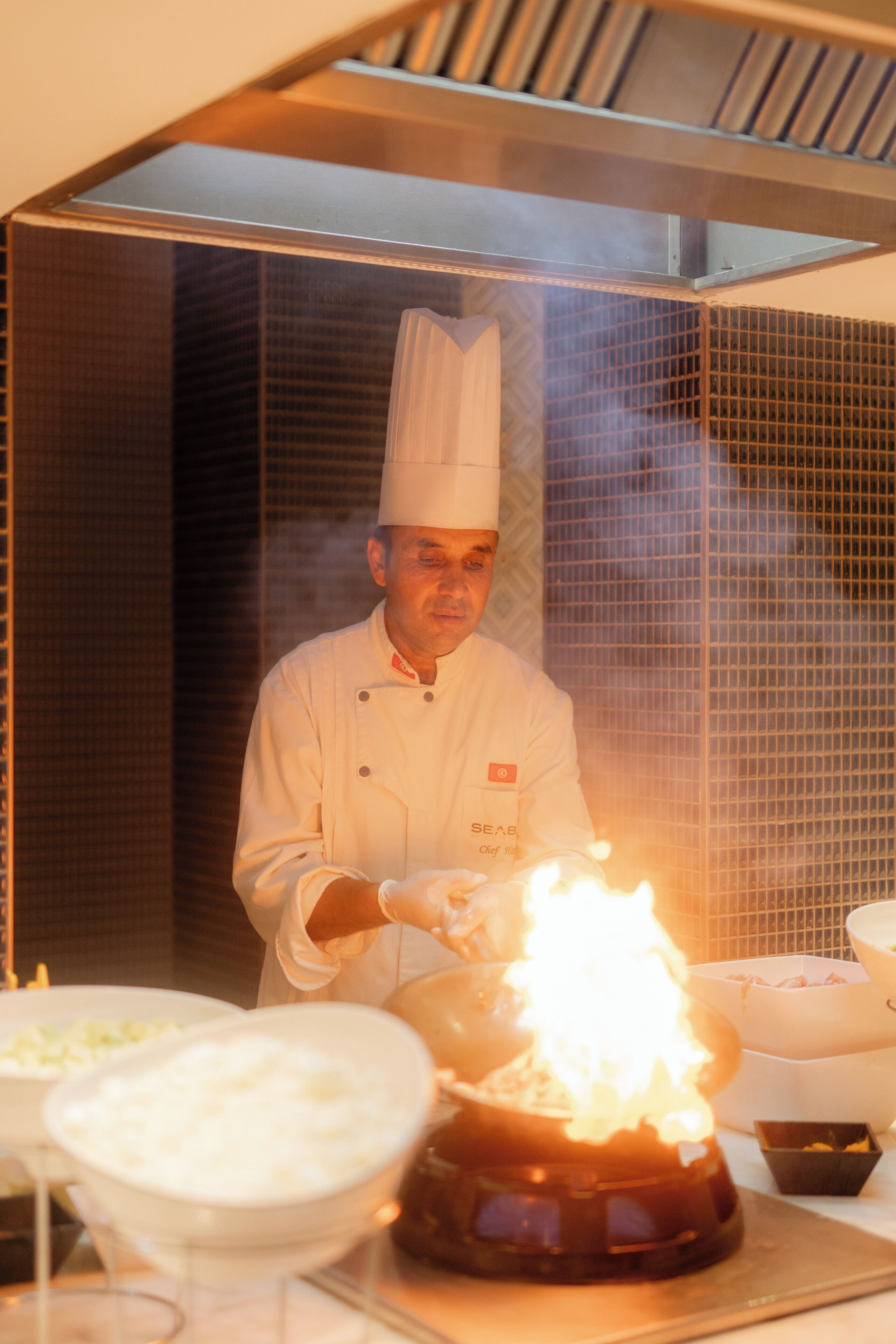 A chef in a professional kitchen with a stove in the foreground.