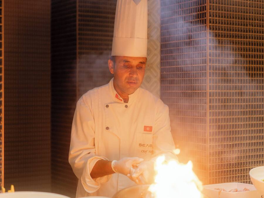 A chef in a professional kitchen with a stove in the foreground.