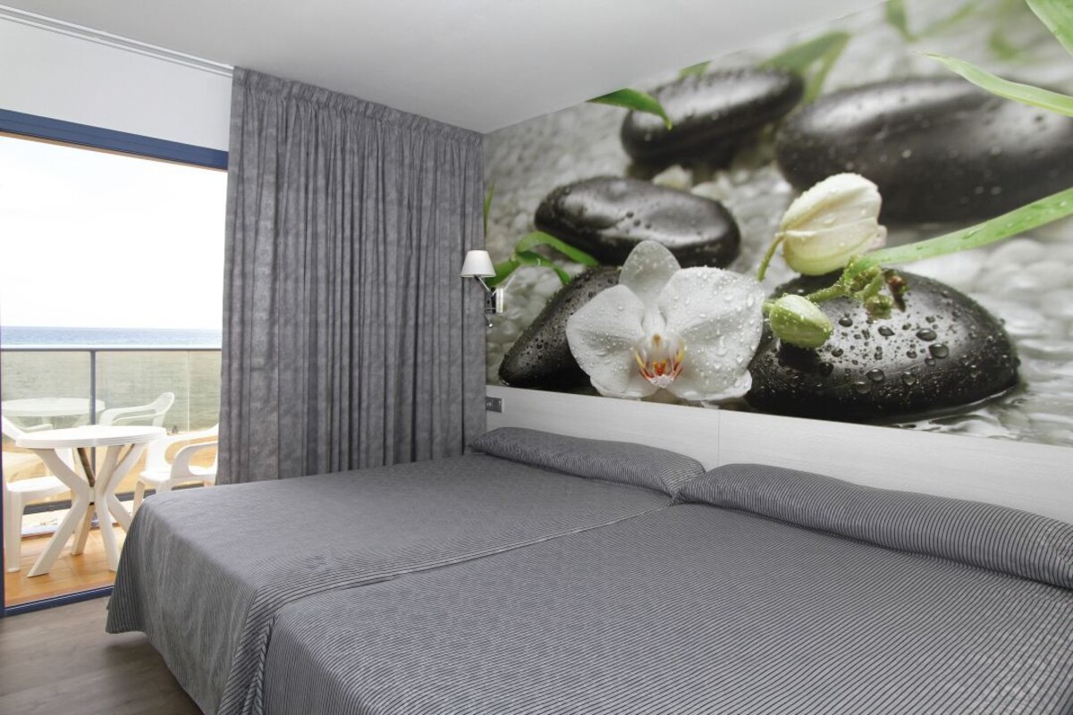Habitación de hotel con cama, vista al mar y un mural en la pared con piedras y flores.