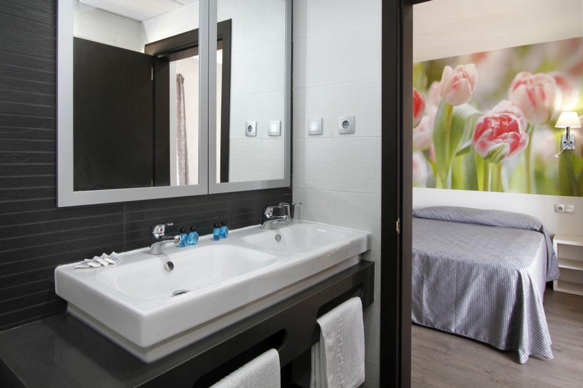 Un baño moderno con dos lavamanos, un espejo grande y una cama con colcha a rayas.