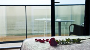 A balcony with a table and a chair, a rose on the table, and a view of the sea. - Hotel Amaraigua - Adults Only (Malgrat de Mar)