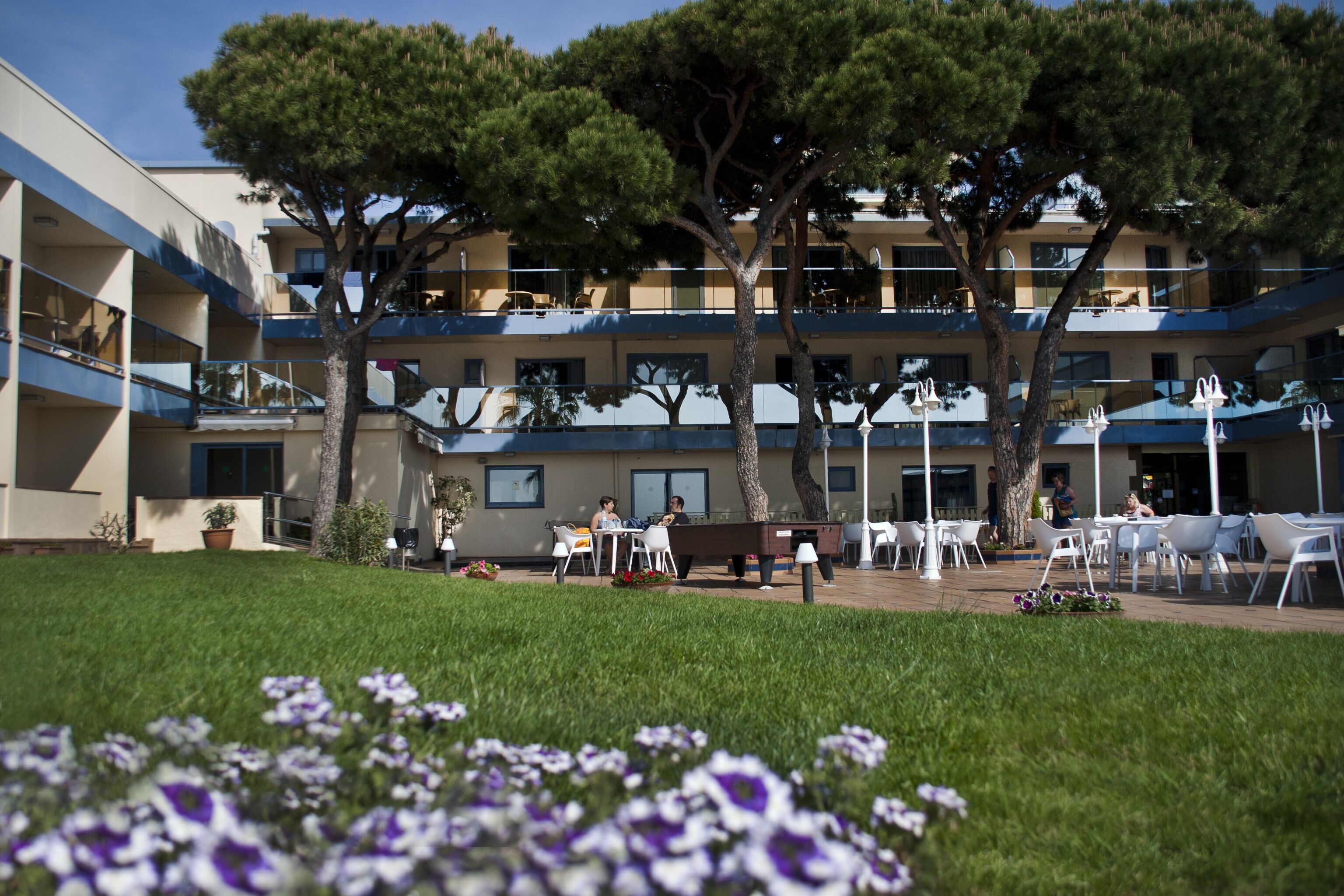 A hotel courtyard with outdoor seating, trees, and a building with balconies.