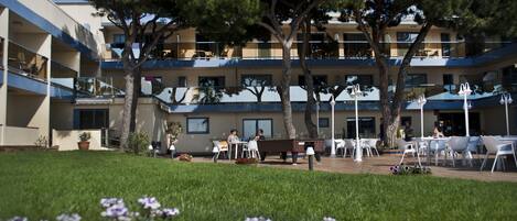 A hotel courtyard with outdoor seating, trees, and a building with balconies.