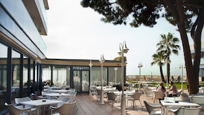 An outdoor patio with tables and chairs, a glass enclosure, and a view of the ocean. - Hotel Amaraigua - Adults Only (Malgrat de Mar)