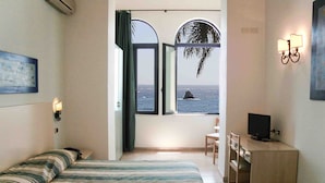 Une chambre avec un lit, un bureau, une chaise, une télévision et une fenêtre donnant sur la mer.