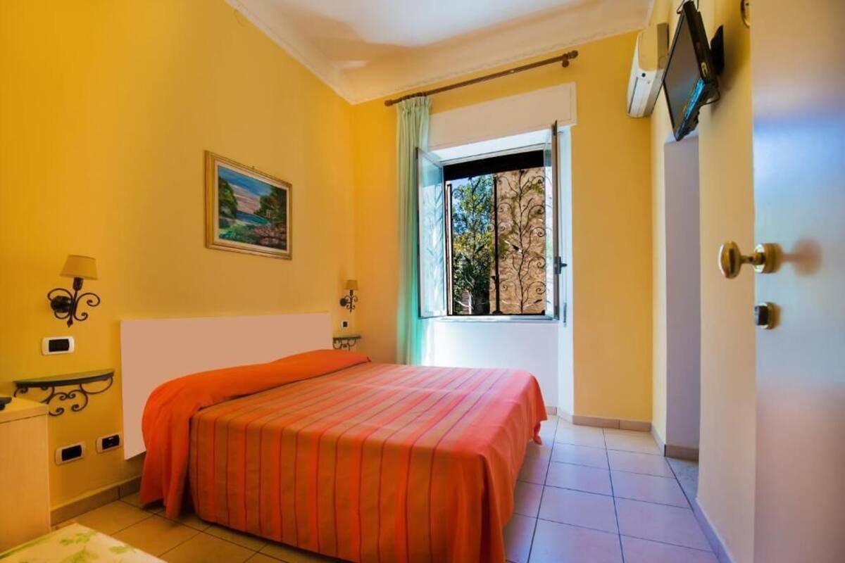 Une chambre à coucher avec un lit, une fenêtre donnant sur des arbres, un tableau accroché au mur et un téléviseur fixé au mur.