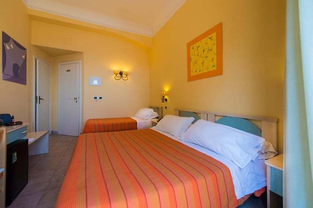 A hotel room with two beds, a desk, a chair, and a door.