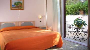 A hotel room with a bed, a painting on the wall, and a balcony with a table and chairs.