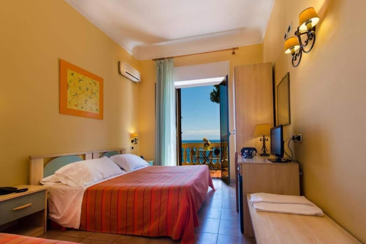 Une chambre d’hôtel avec un lit, un bureau équipé d’un ordinateur, une chaise et une vue sur la mer.