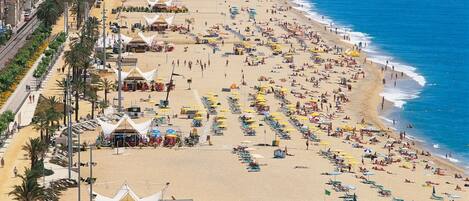 A beach with numerous umbrellas and sunbeds, a clear sky, and a calm sea.