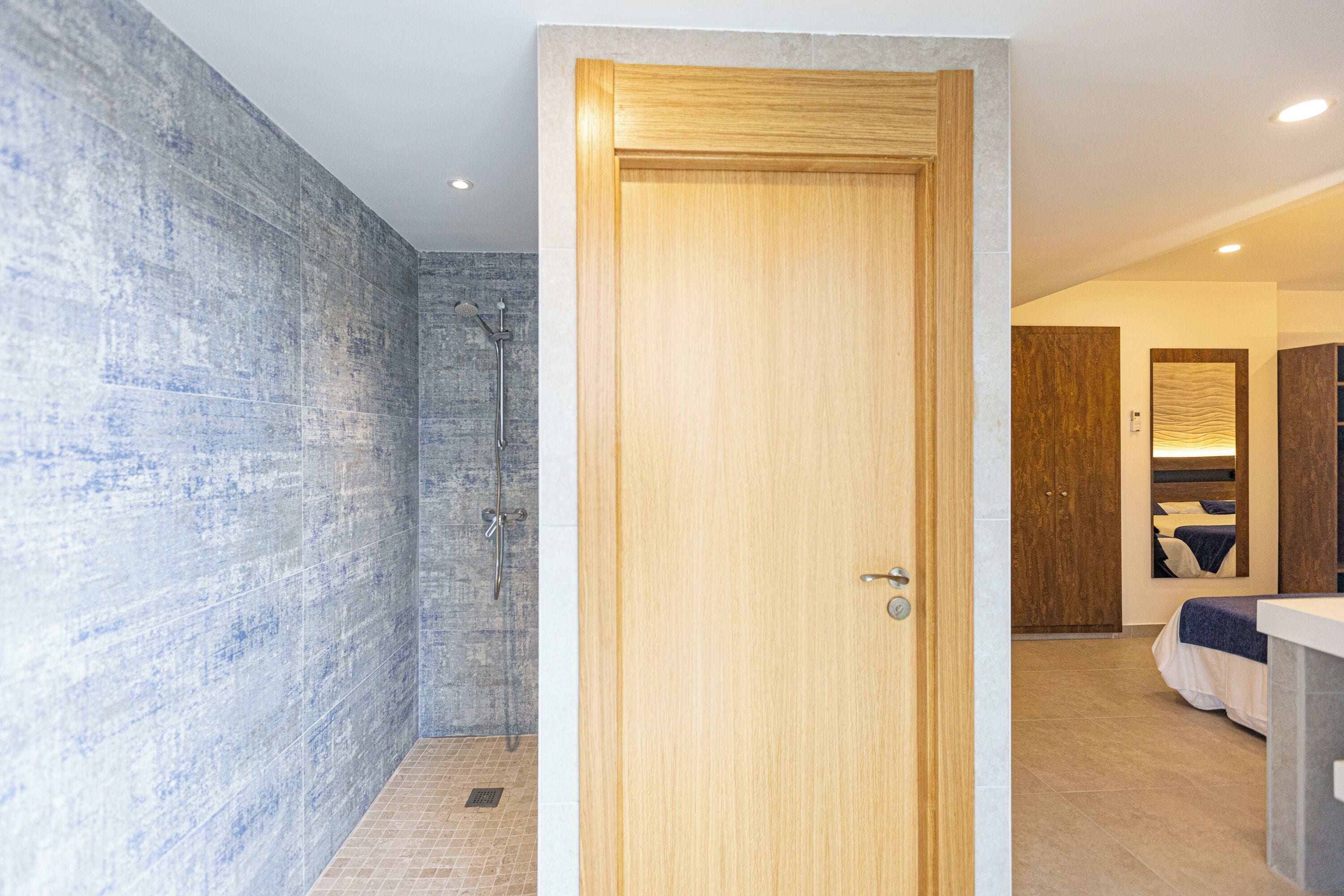 Un baño moderno con ducha, puerta de madera y una cama en la habitación contigua.