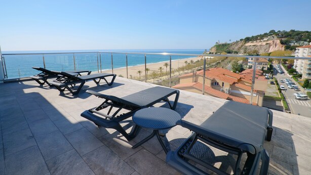Terraço com mesas de piquenique com vista para uma praia e uma cidade costeira.