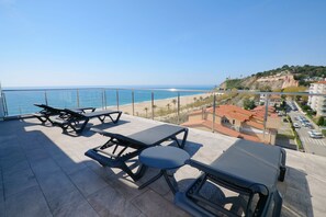 A terrace with picnic tables overlooking a beach and a coastal town. - Hotel Internacional (Calella)