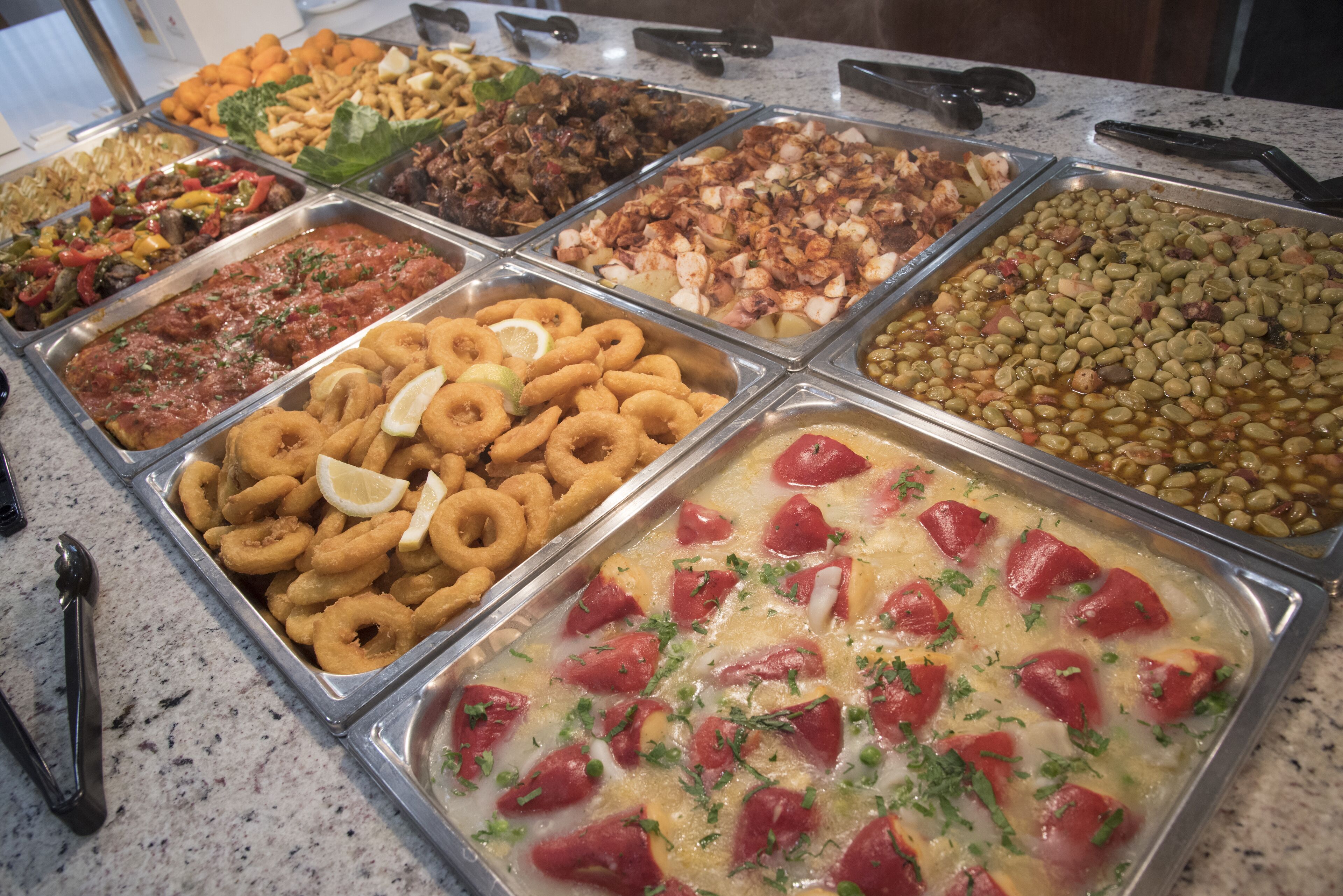 Un bufé con diversas opciones de comida, incluyendo frituras, ensaladas y un plato de pasta.