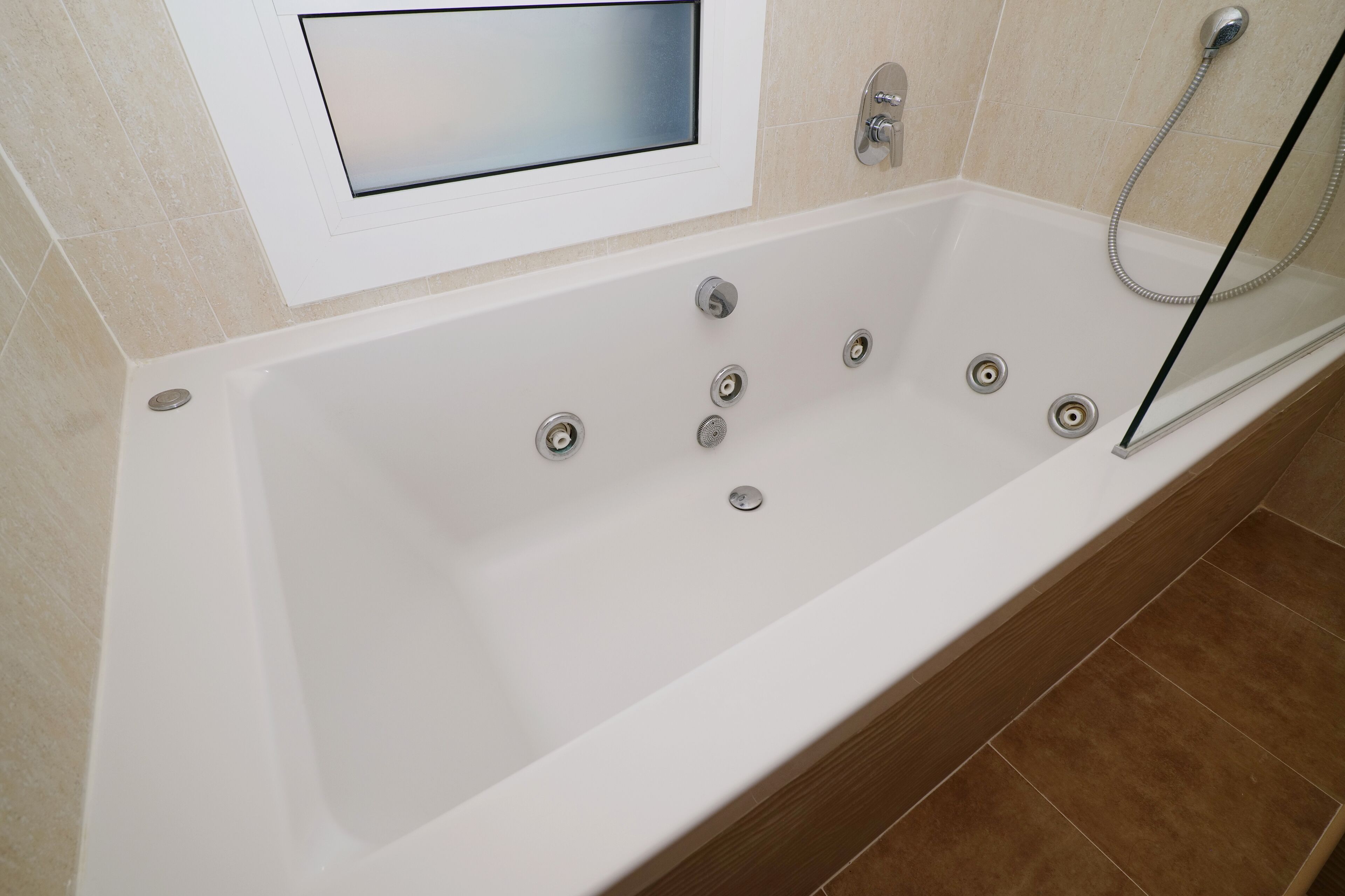 Un bagno moderno con una vasca da bagno bianca, un soffione doccia estraibile e una finestra integrata sopra la vasca.
