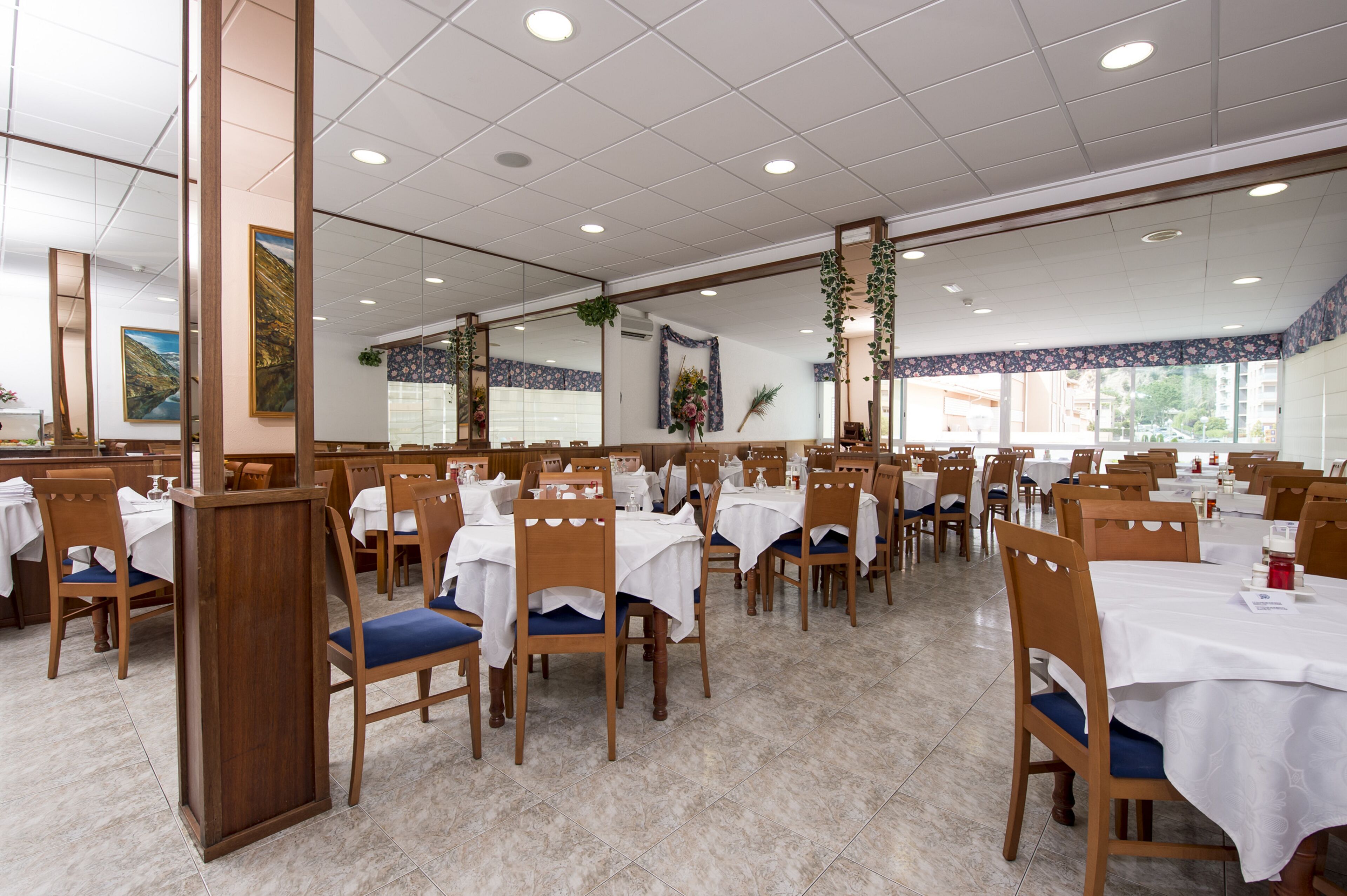 Un vaste espace dédié à la salle à manger, avec de nombreuses tables et chaises, de grandes fenêtres et un sol carrelé.