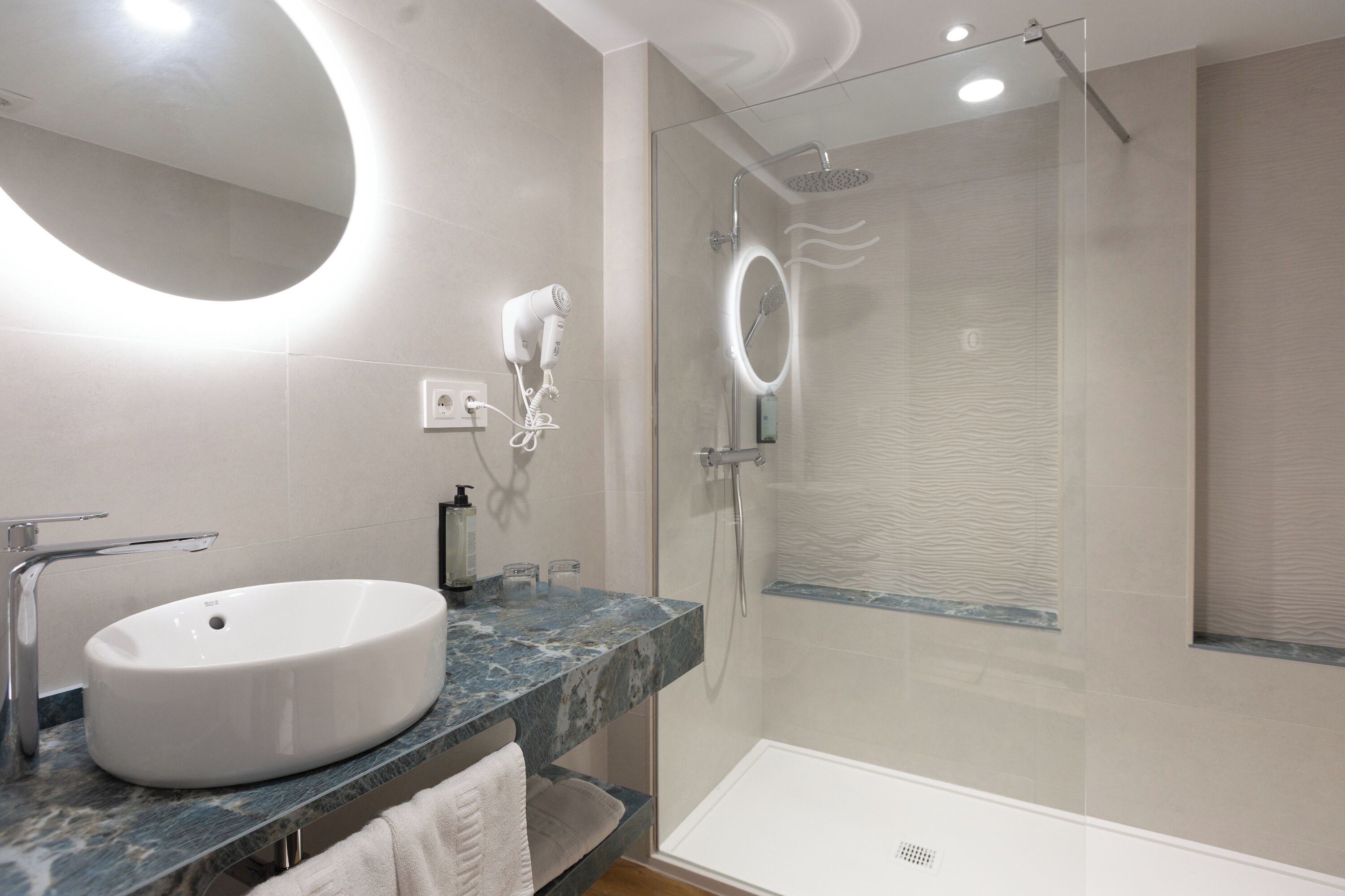 A modern bathroom with a round mirror, a white sink, and a glass-enclosed shower.