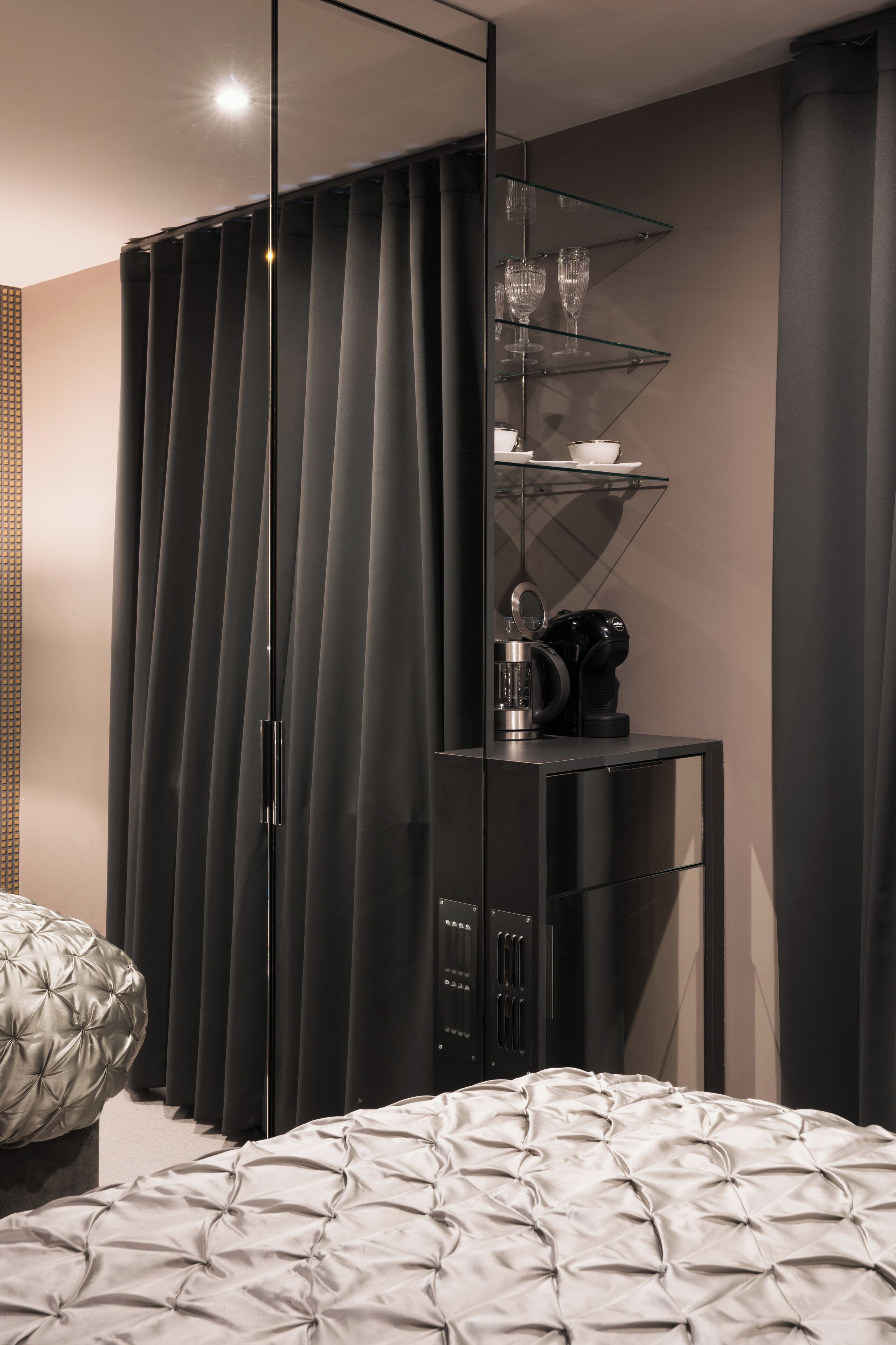 A modern bedroom with a large bed, a wardrobe, and a small table with a kettle and cups.