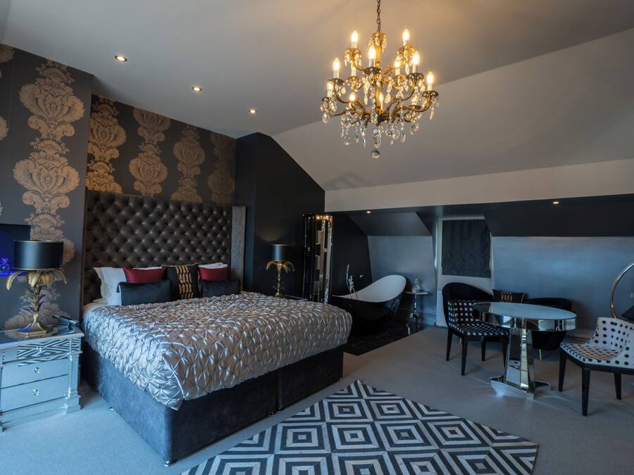 A modern bedroom with a large bed, a chandelier, a vanity, and a seating area with a table and chairs.