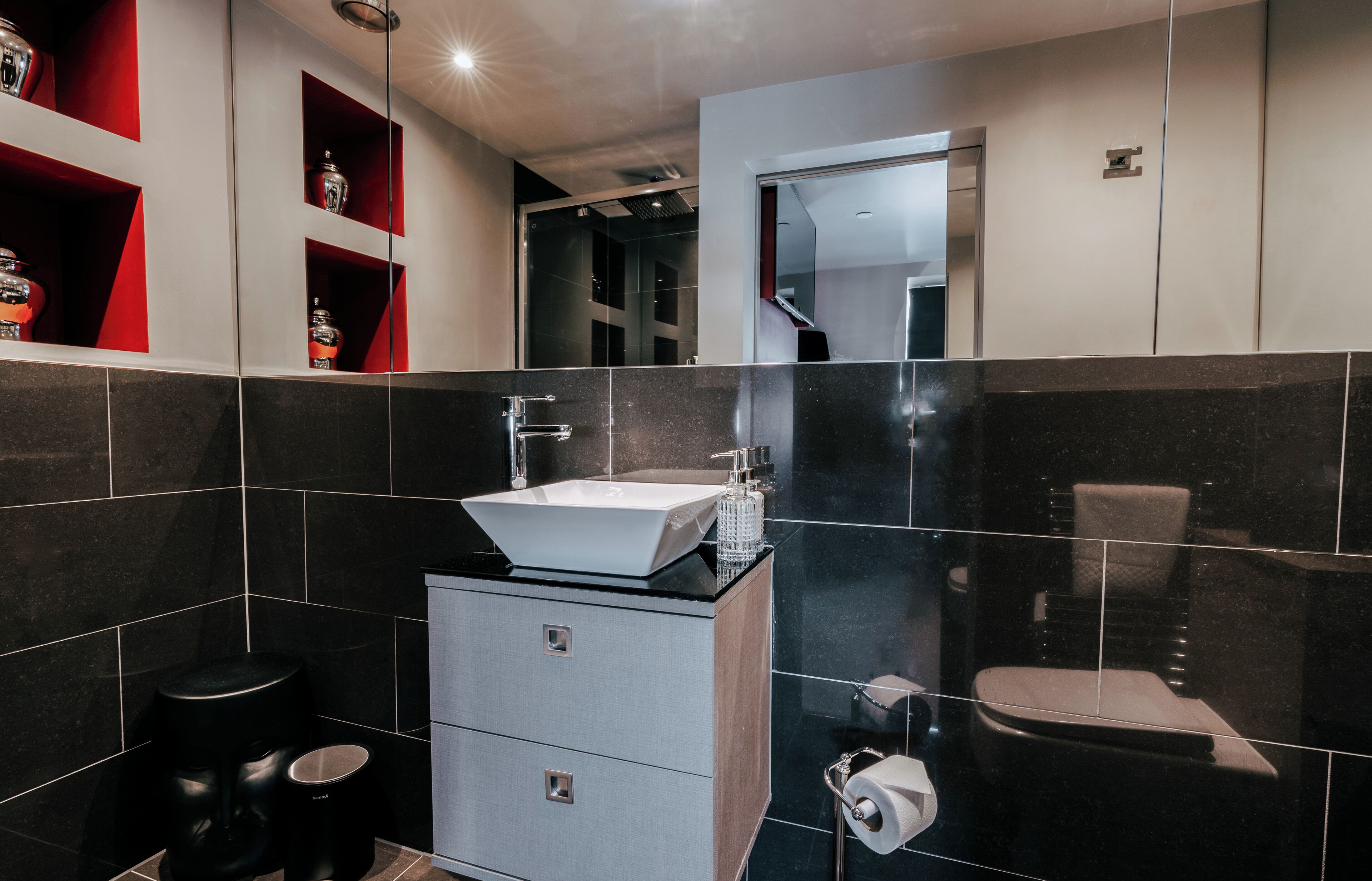A modern bathroom with a white sink, black tiles, a mirror, and a toilet.
