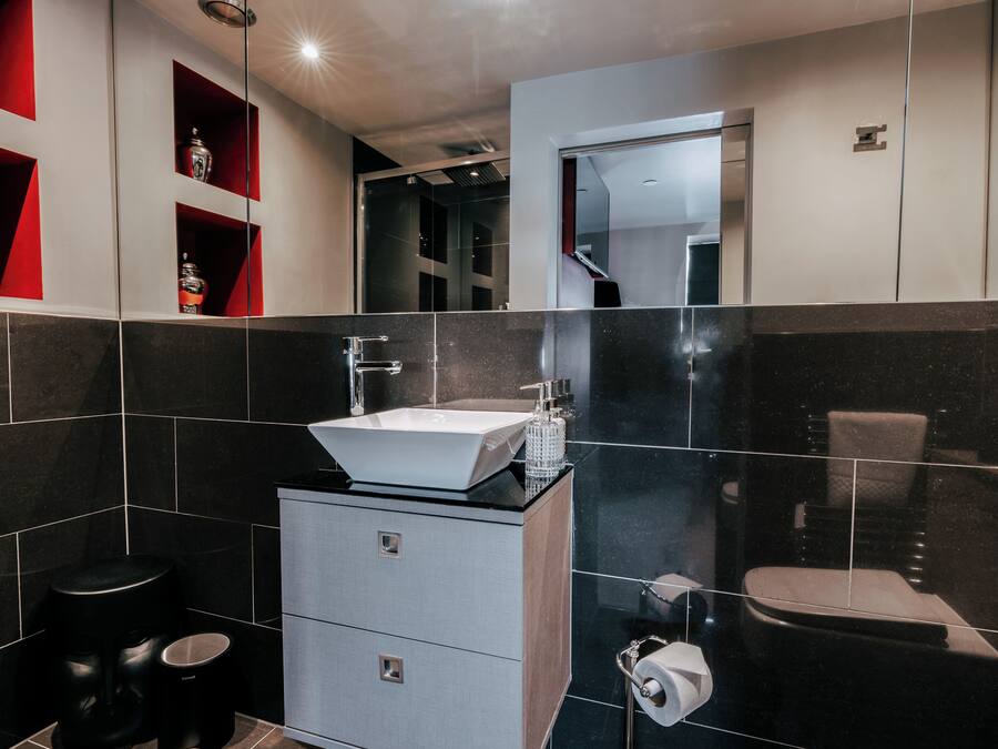 A modern bathroom with a white sink, black tiles, a mirror, and a toilet.