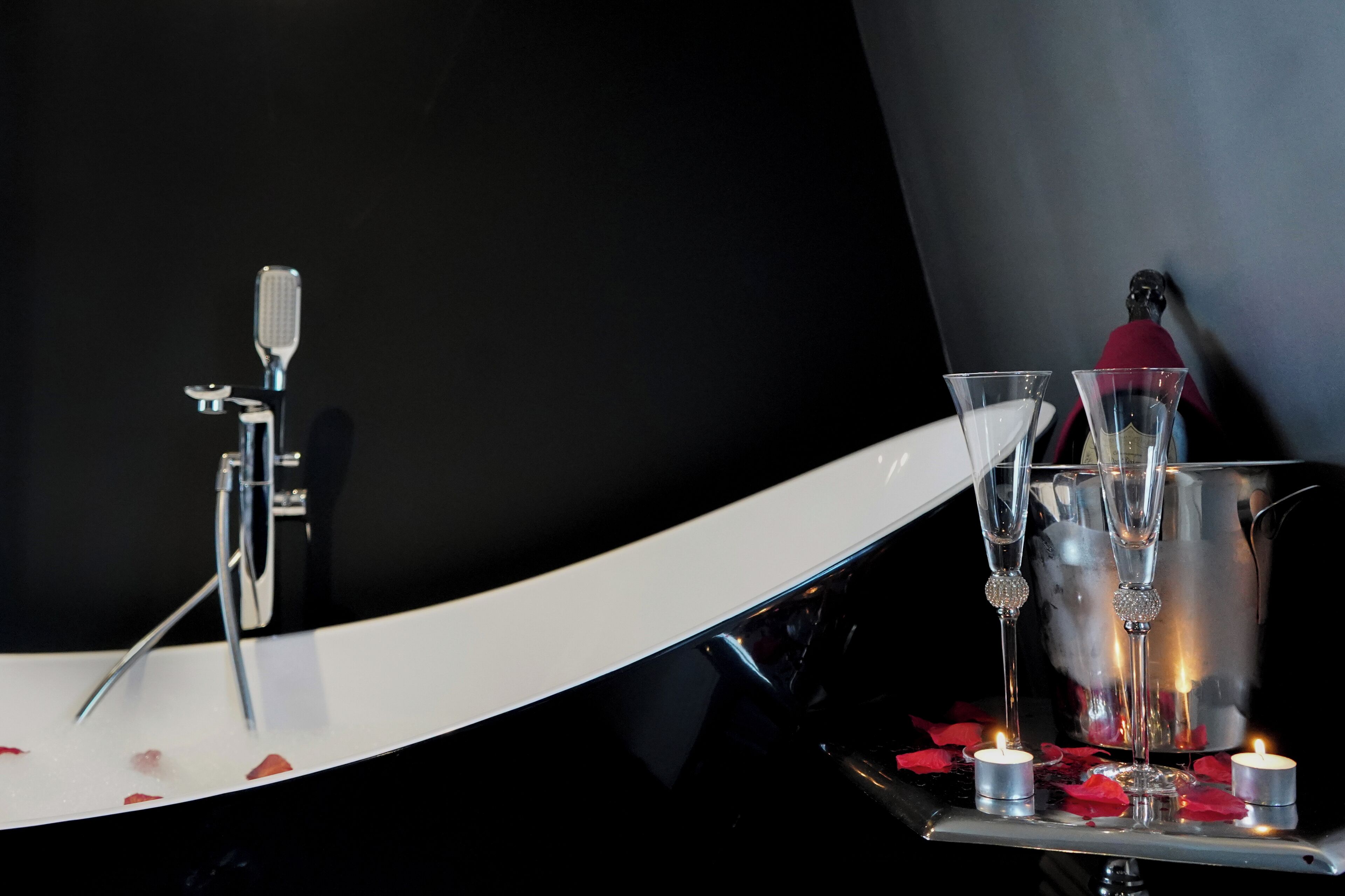 A bathtub with rose petals, champagne flutes, and candles.