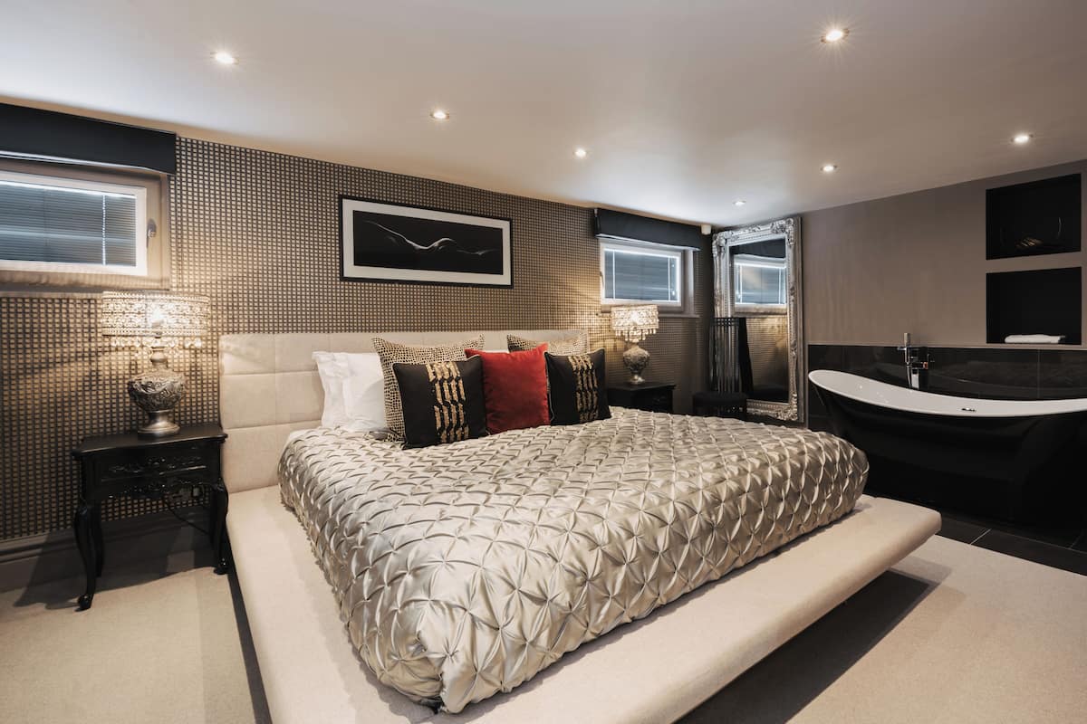 A modern bedroom with a large bed, a built-in bathtub, and a large mirror.