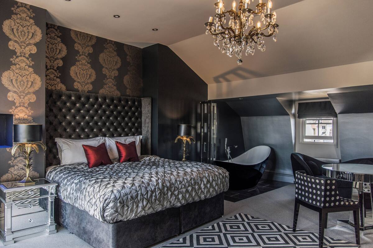 A modern bedroom with a tufted headboard, a large bed, a chandelier, and a dining area with a chair and table.