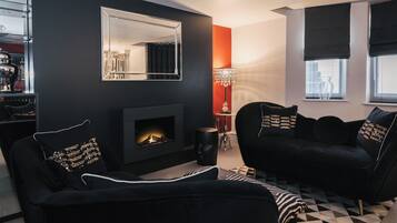 A modern living room with a fireplace, black sofas with gold accents, a large mirror, and a geometric patterned rug.