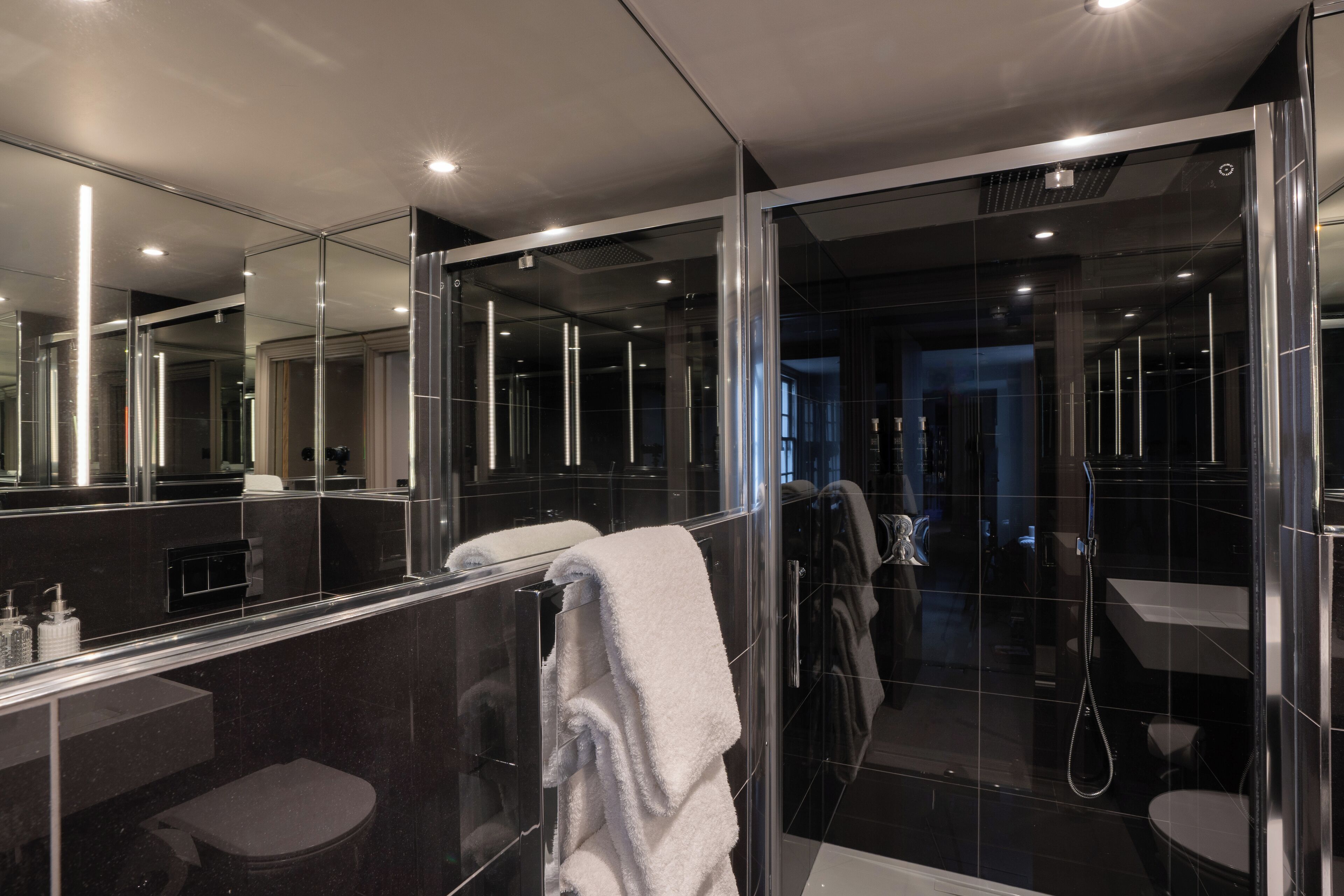Une salle de bain moderne avec une douche à parois de verre, un grand miroir et un porte-serviettes.