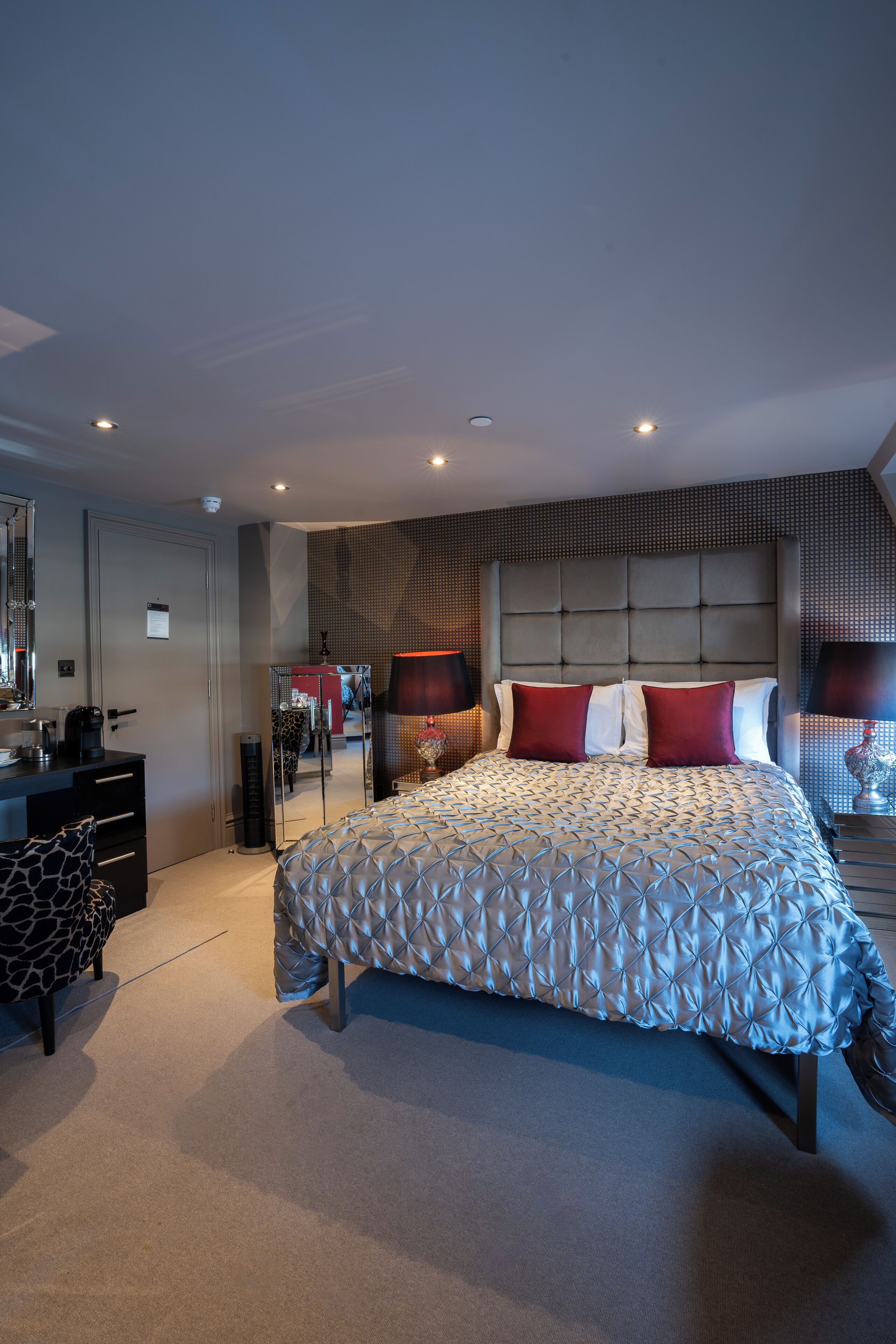 A modern bedroom with a large bed, a dresser, a mirror, and a desk.